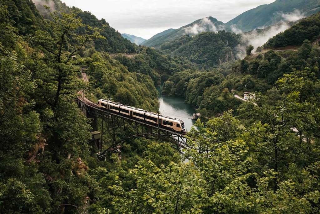 Centovalli Railway train crossing a high bridge through a green Alpine valley
