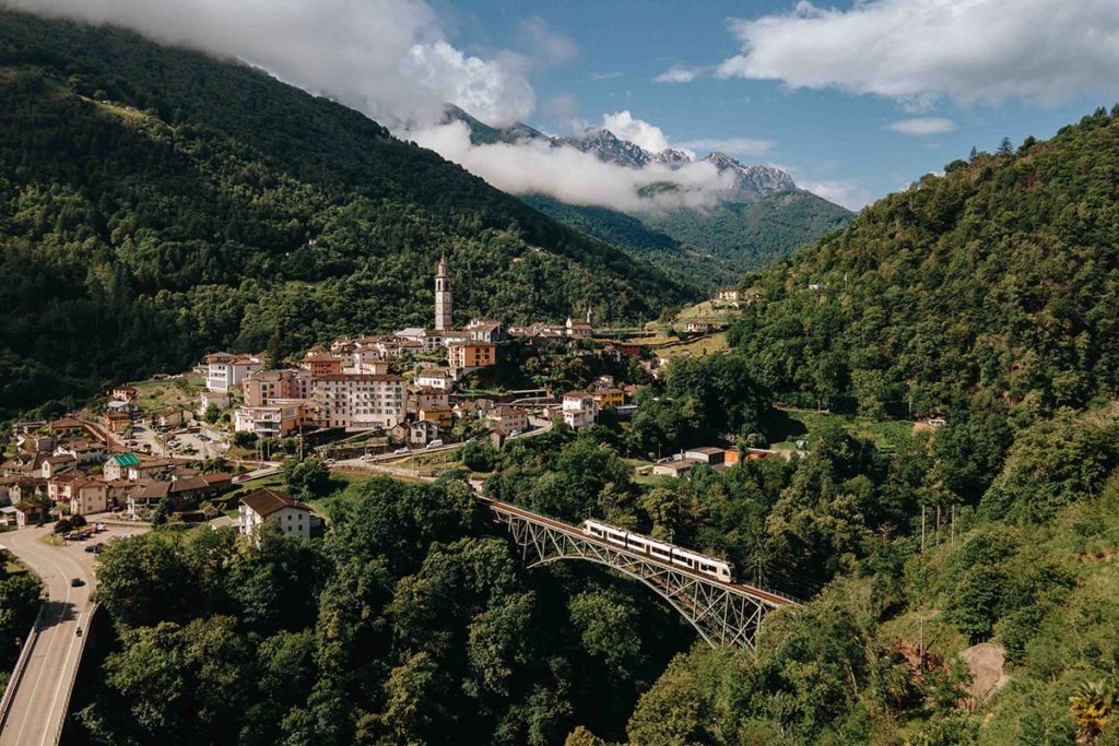 Centovalli Railway train crossing a viaduct beside a mountain village in the Alps